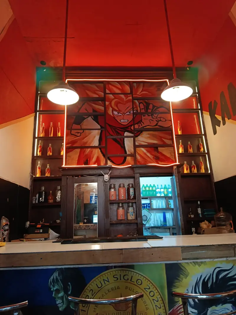 Barra roja con un mural de una figura en llamas, dos lámparas colgantes y repisas con botellas