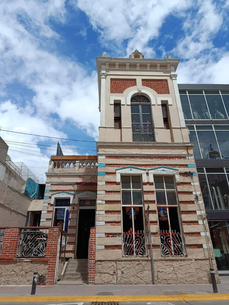Fachada de la casona con franjas de ladrillo rojo y cantera y una torre al centro