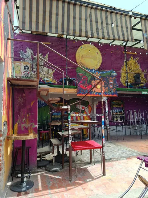 Patio de la planta alta con muros morados pintados, un sol amarillo, estandarte de luchadores y mesas altas